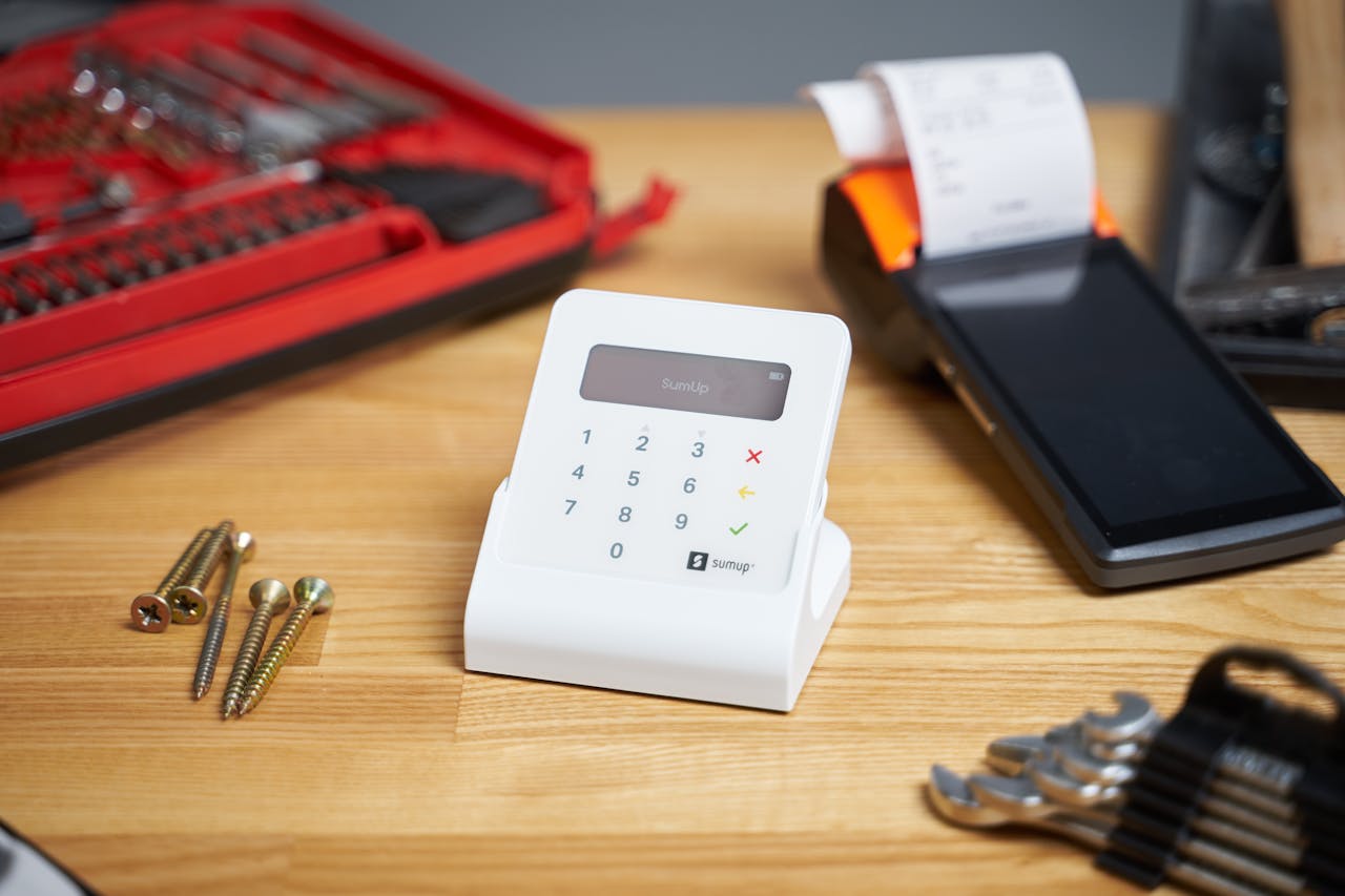 Selective focus of white contemporary calculator surrounded by cash register and tools for repair and building on beige wooden table in bright room